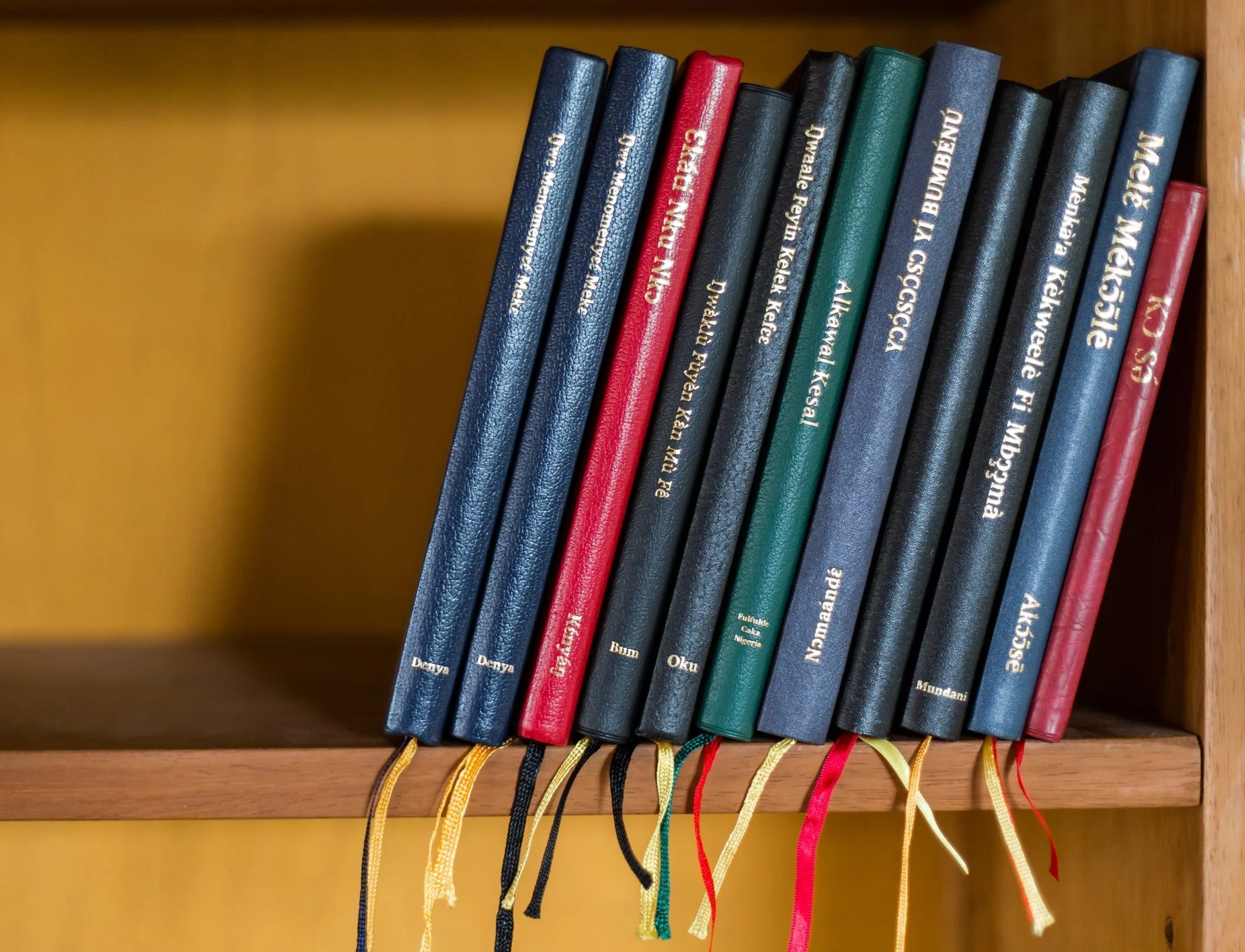 A shelf holding copies of ten New Testaments from Cameroon (and one from Nigeria) completed by, or in cooperation with, Cameroon Association for Bible Translation and Literacy (CABTAL)