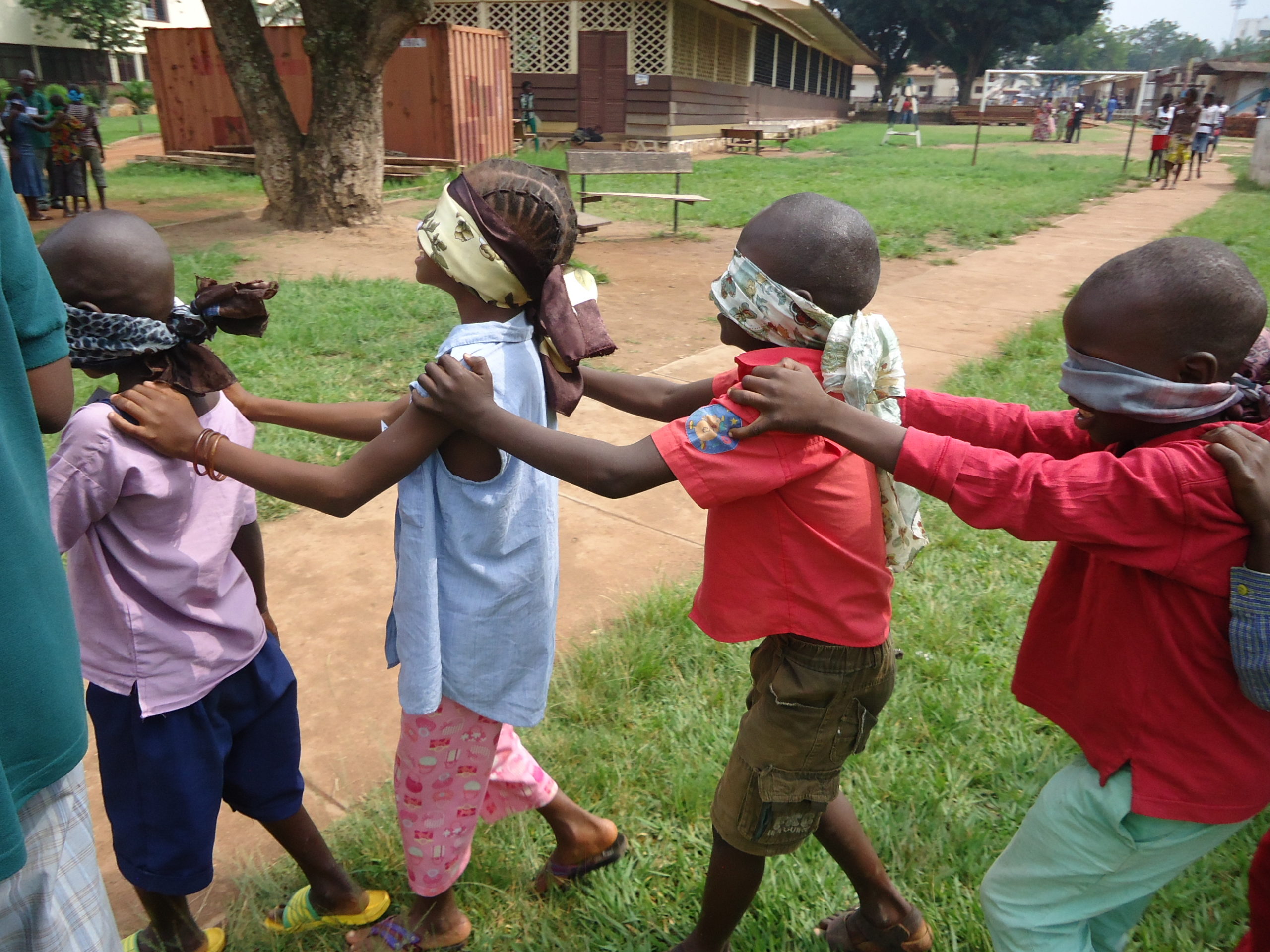 Children, blindfolded, play a game, walking with their hands on each others' shoulders