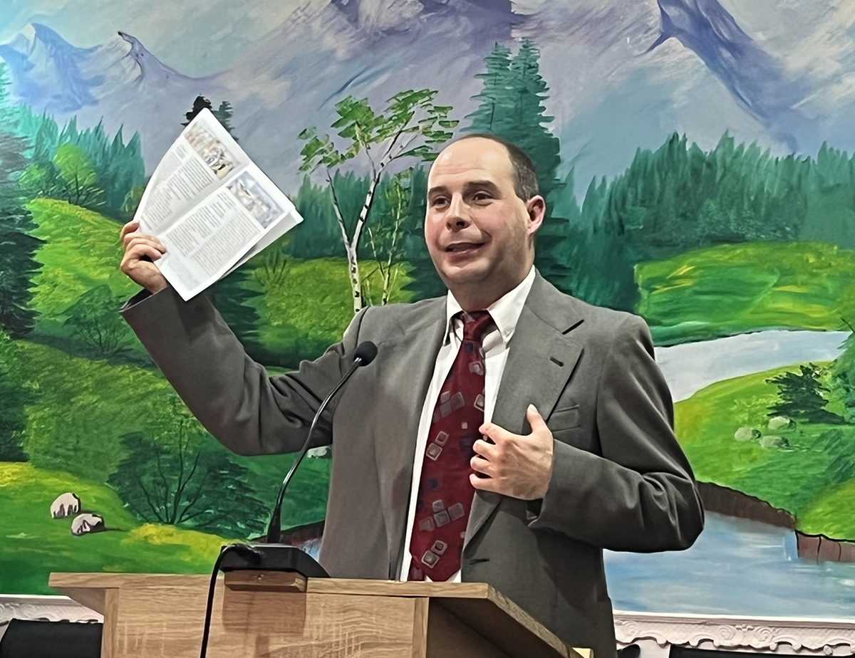 Image of Wycliffe Romania worker Zoltan presenting a booklet with the Standard Romani translation of John 18–21 to a Roma church in Romania