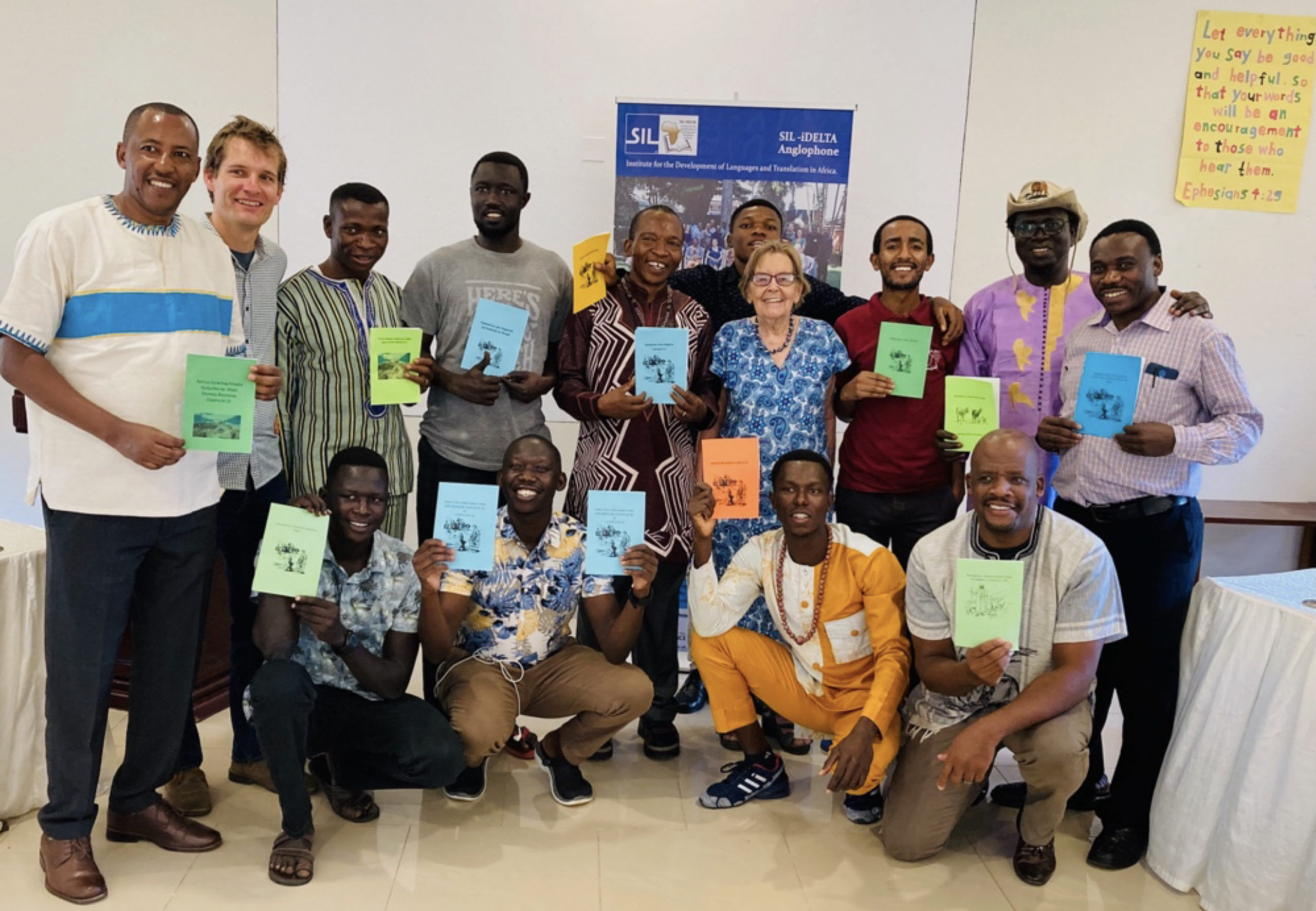 Image of Margaret Hill with students at an August 2023 translation workshop in Uganda, holding the Bible study books they wrote in their own languages during the workshop